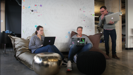 People sitting in formal bean bag chairs, discussing their laptops in front of a wall of logos.