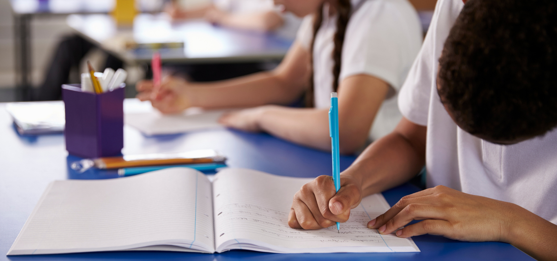 Primary school students writing in a notebook.